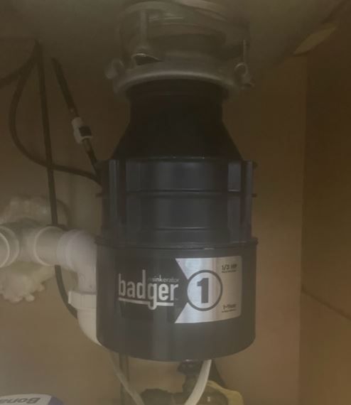 Black Badger 1 garbage disposal under a kitchen sink, with white pipes.