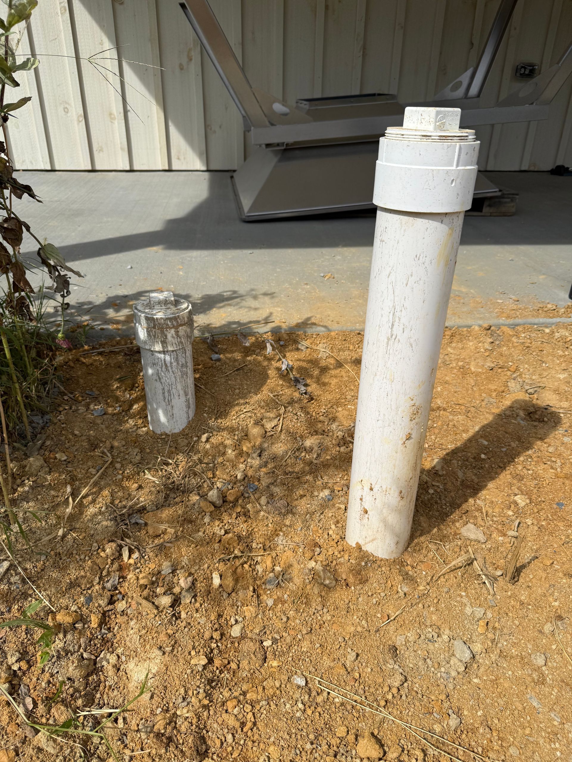 Two white pipes emerging from dirt, near a building.