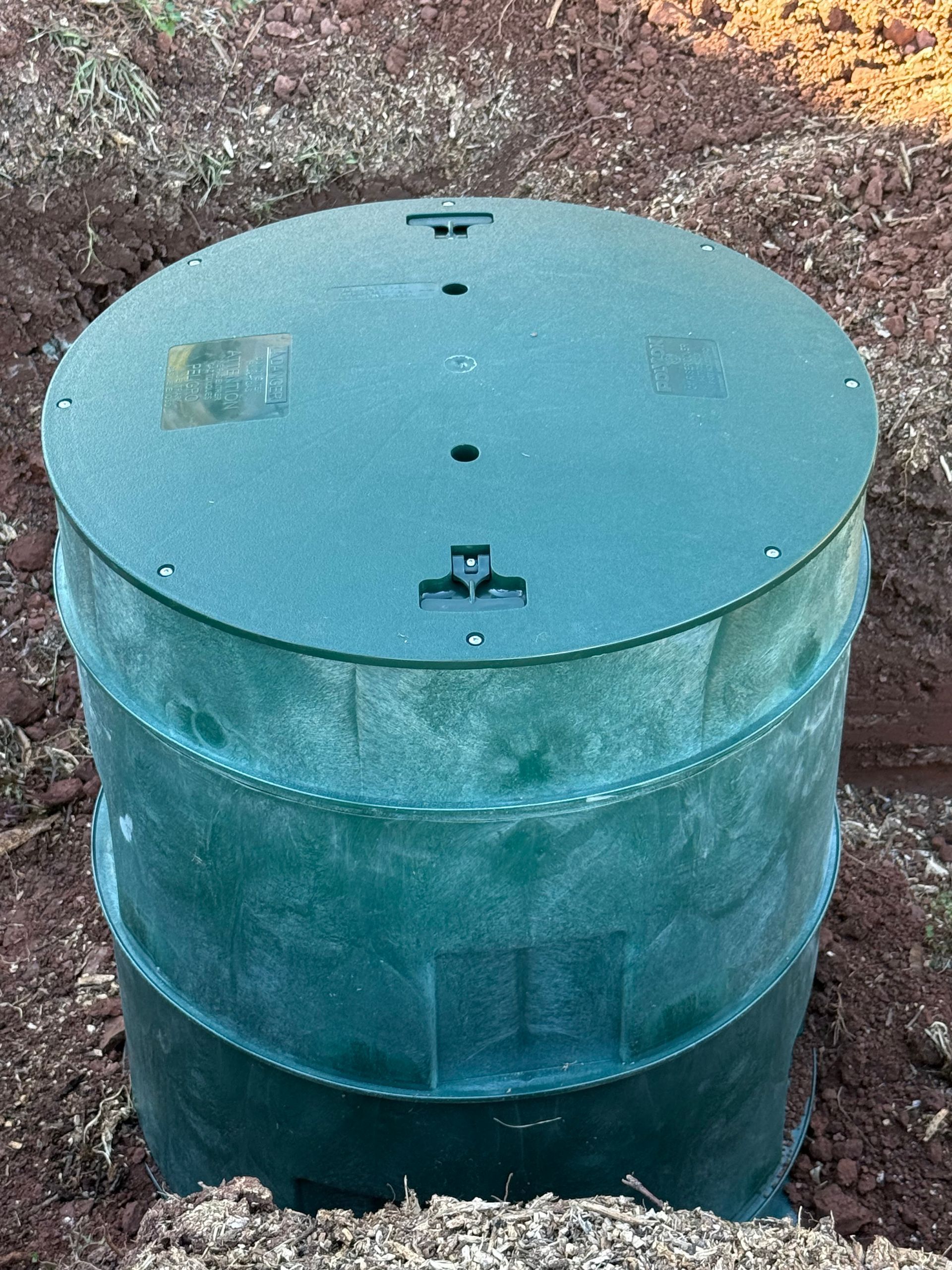 Green septic tank in the ground with a round lid.