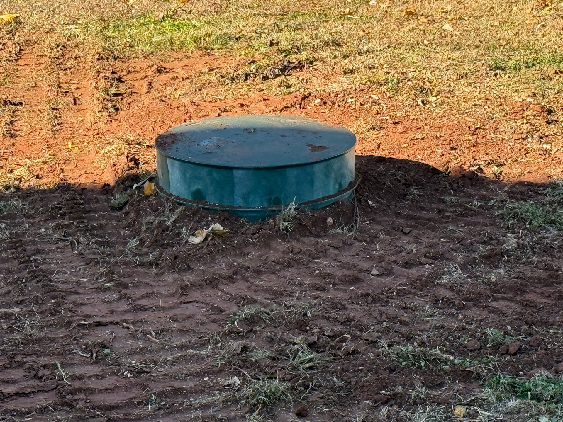Green septic tank lid in a dirt yard.