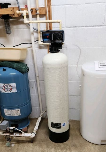 Water softener system in a basement setting with plumbing and pressure tank visible.