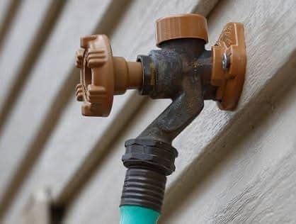 Brown and metal outdoor water faucet on a house, with a green hose attached.