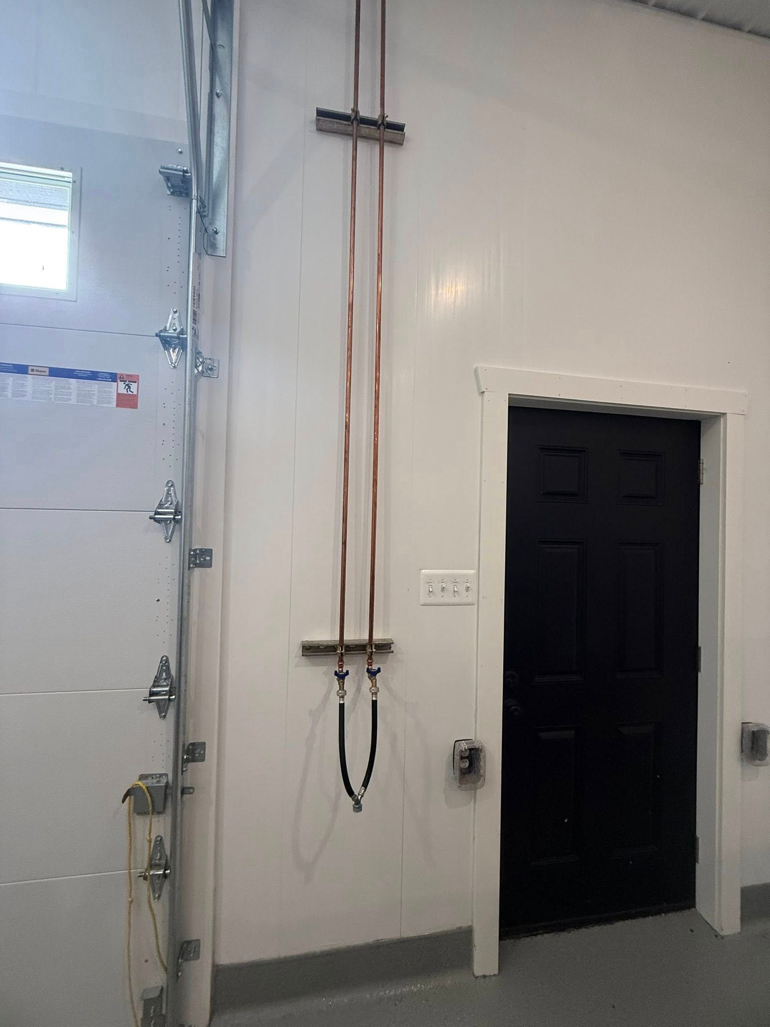 Copper pipes mounted on a white wall in a room with a black door and garage door.