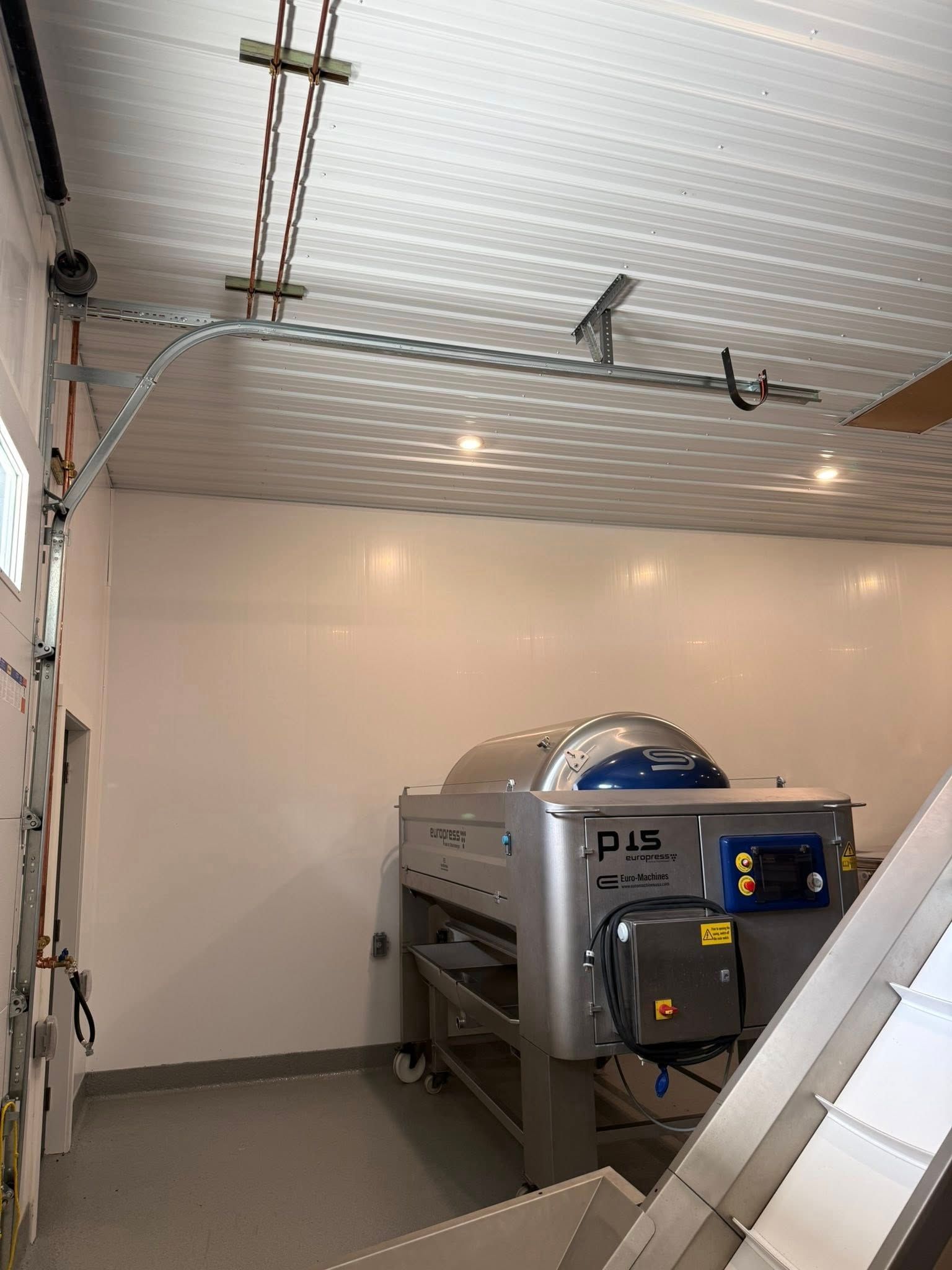 Interior view of a food processing facility with equipment; white walls and ceiling; overhead garage door track.