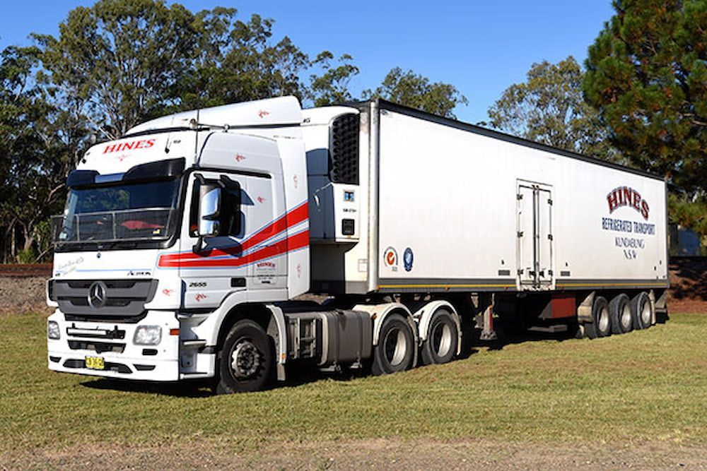 White Semi-truck With Red Stripes Parked on Grass — Hines Refrigerated Transport Pty Ltd in Kundabung, NSW