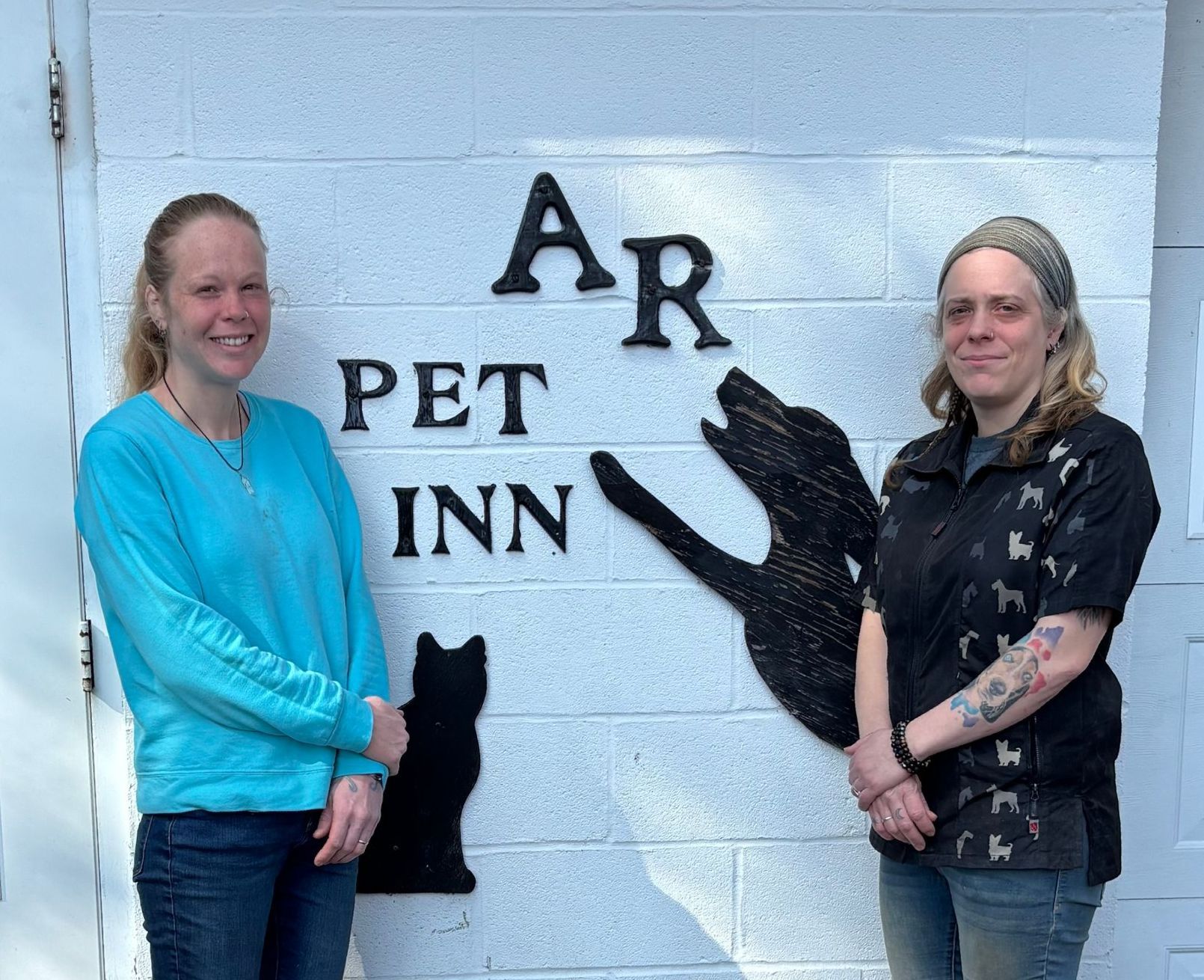Two women are standing in front of a pet inn sign.