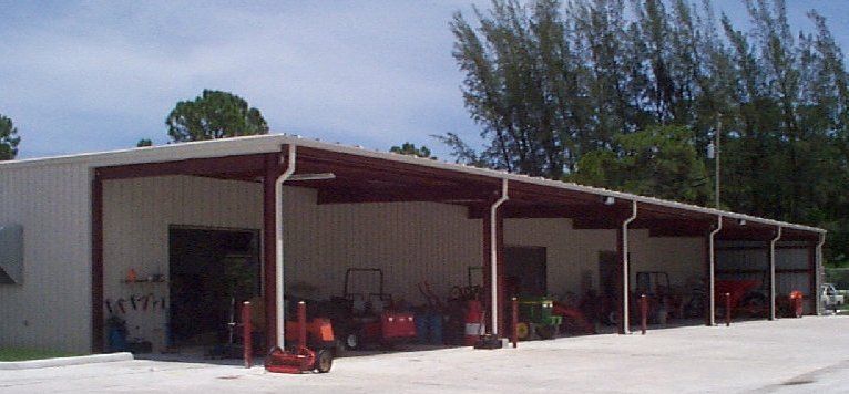 A row of tractors are parked under a covered shed