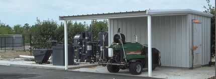 A green lawn mower is parked under a shed.