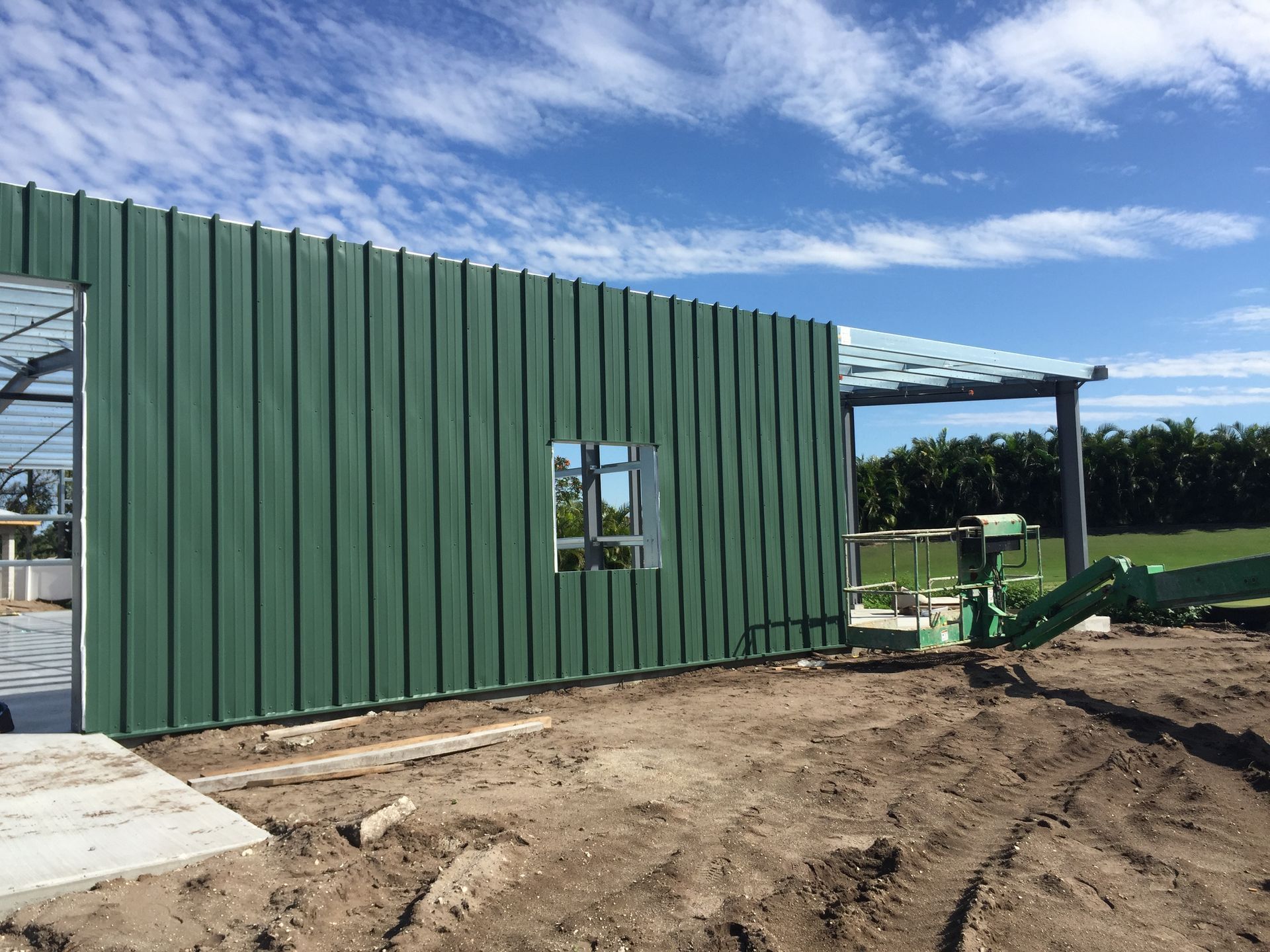 A green building is being built on a dirt field.