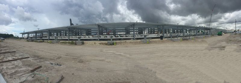 A large building is being built in the middle of a dirt field.