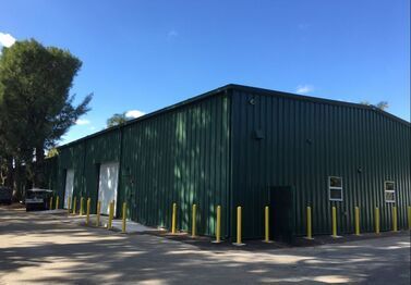 A large green metal building with yellow poles in front of it.