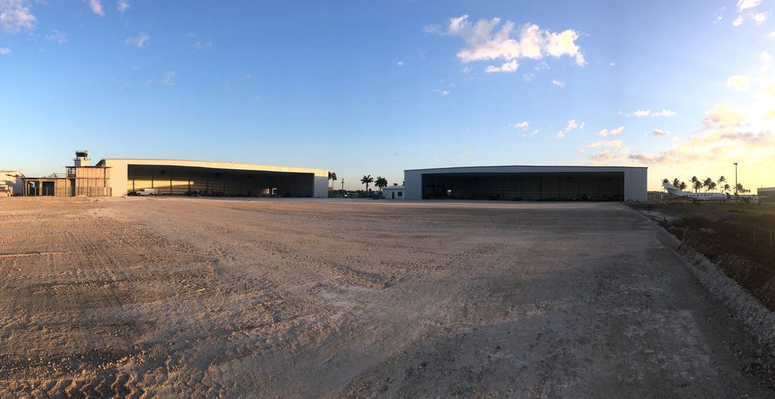A dirt road leading to a large building with a blue sky in the background.