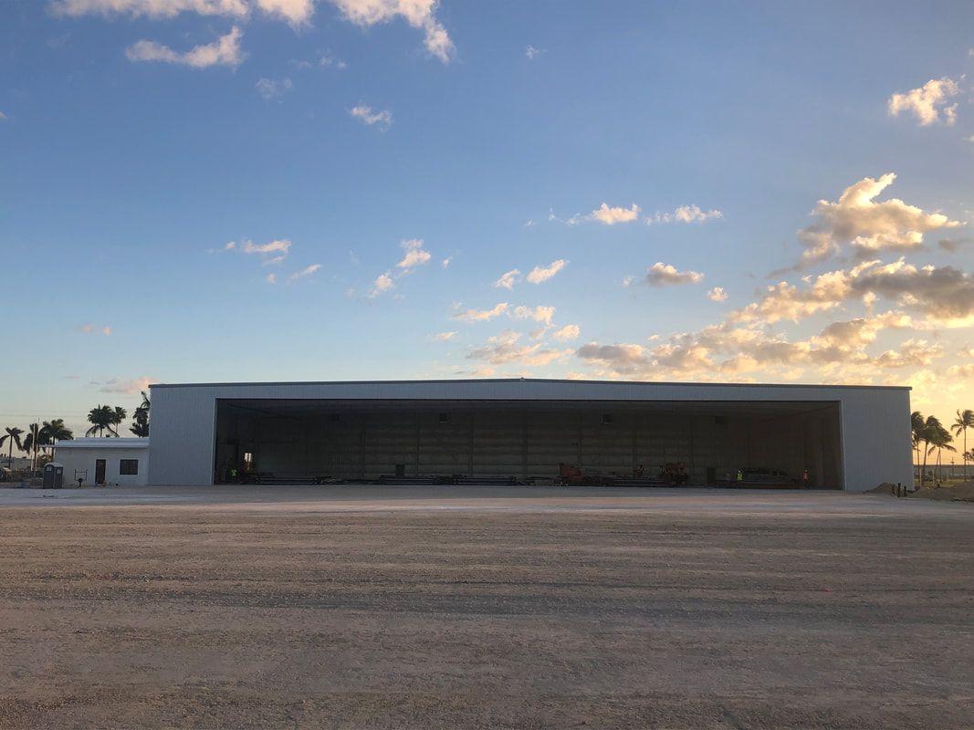 A large white building with a large sliding door is sitting on top of a dirt field.