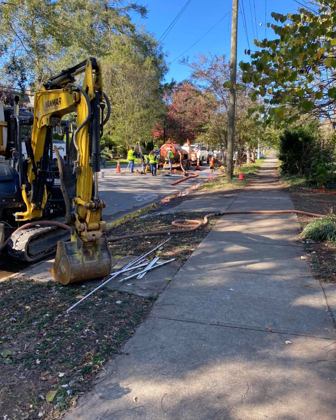 A yellow excavator is parked on the side of the road next to a sidewalk.