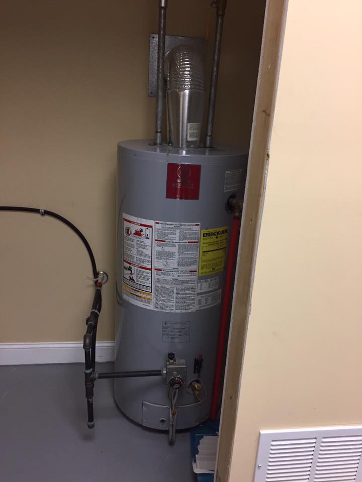 A water heater is sitting in a corner of a room next to a wall.