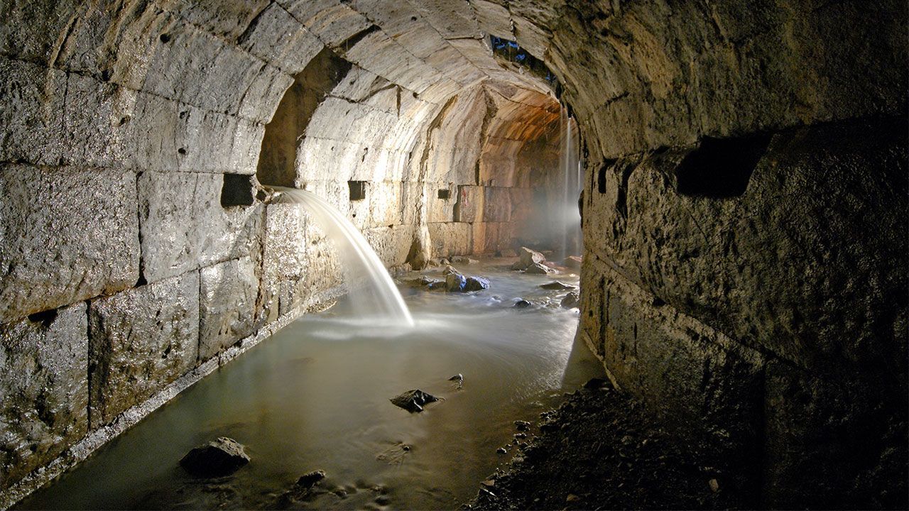 A brick tunnel with a stream of water coming out of it.