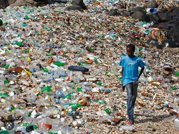 A boy in a blue shirt is walking through a pile of trash