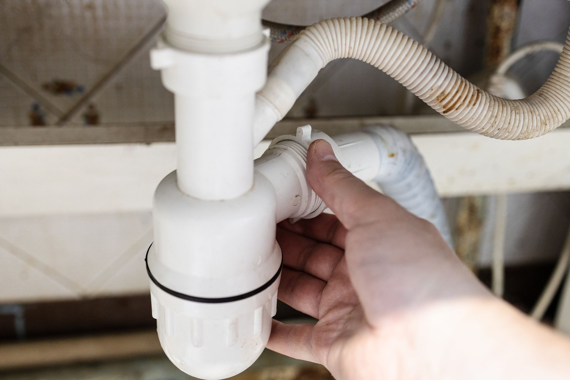 A person is fixing a sink drain with their hand.