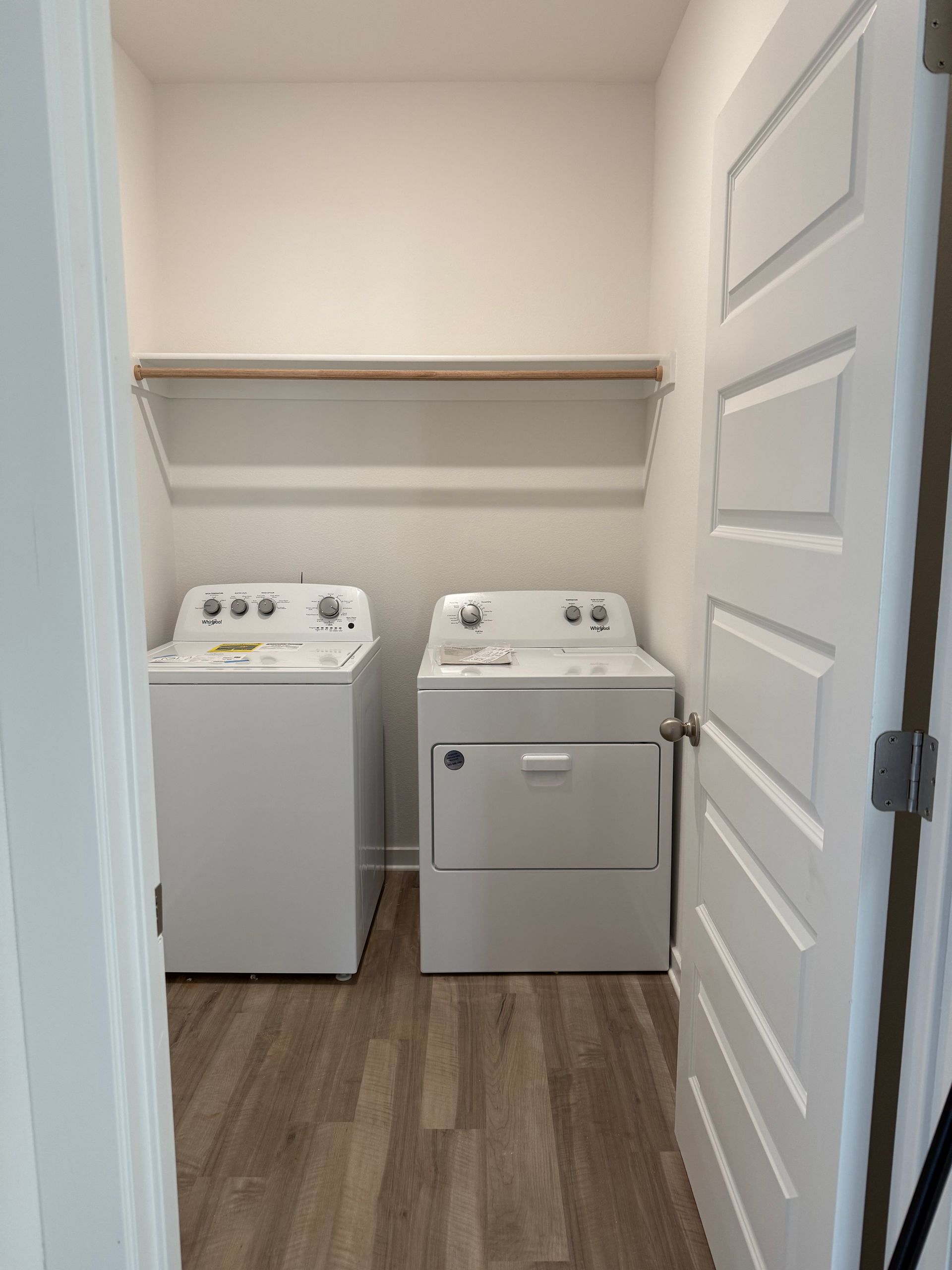 Laundry room with white washer and dryer, wooden shelf, and wooden floor.