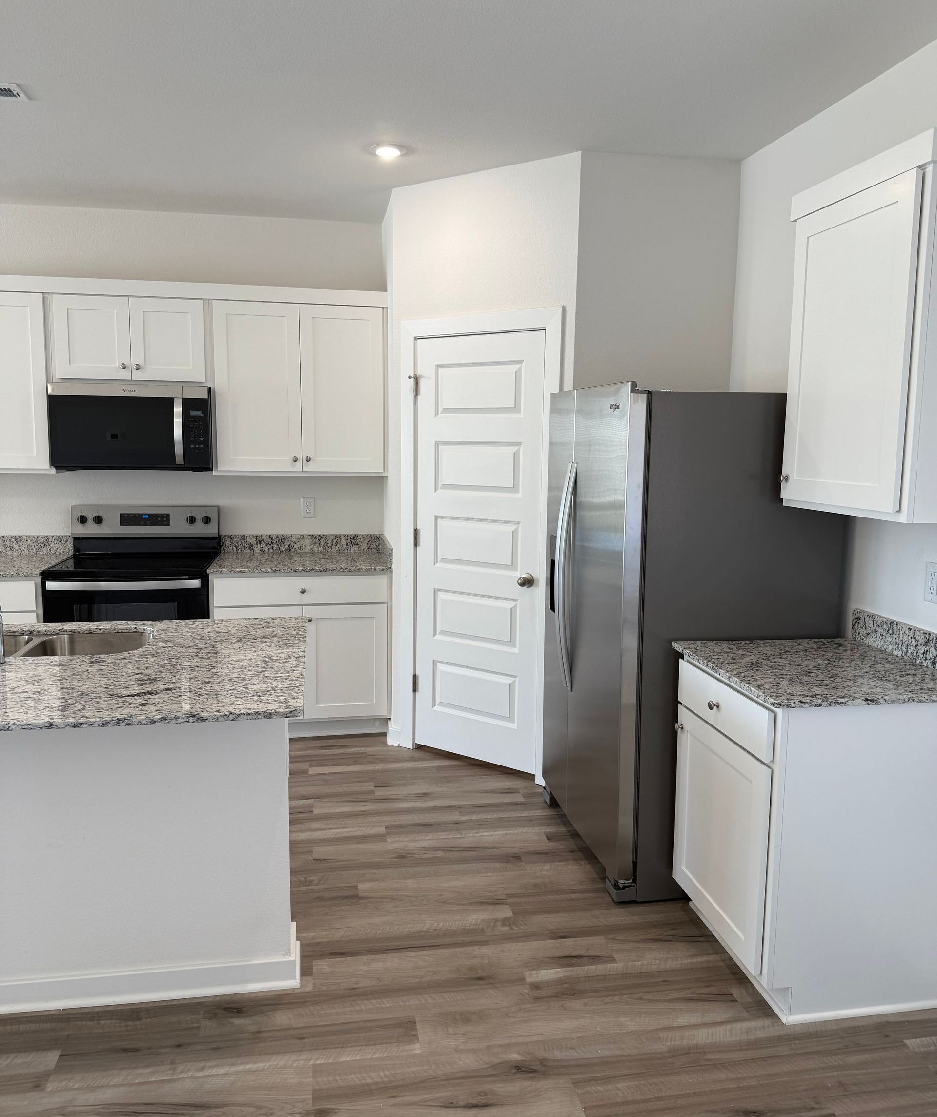 Bright kitchen with white cabinets, stainless steel refrigerator, granite countertops, and wood-look flooring.