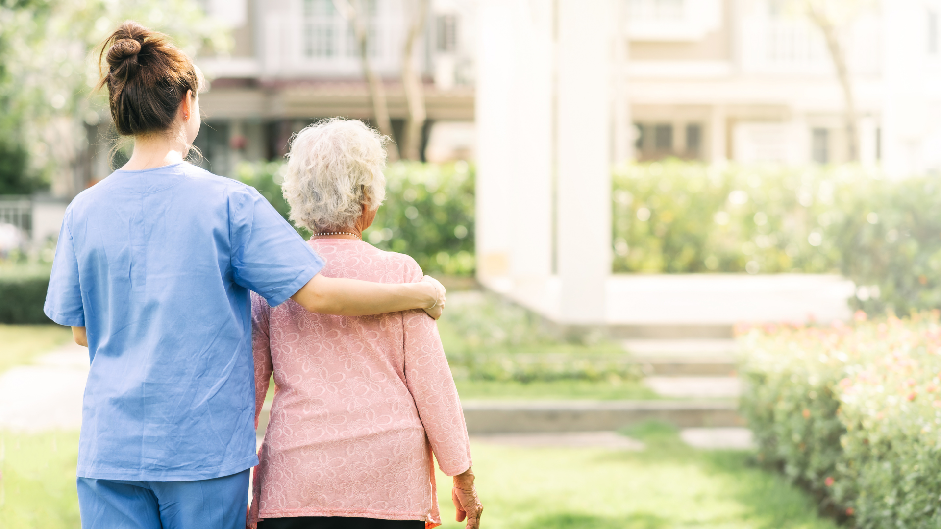 A nurse is walking with an elderly woman in a park.