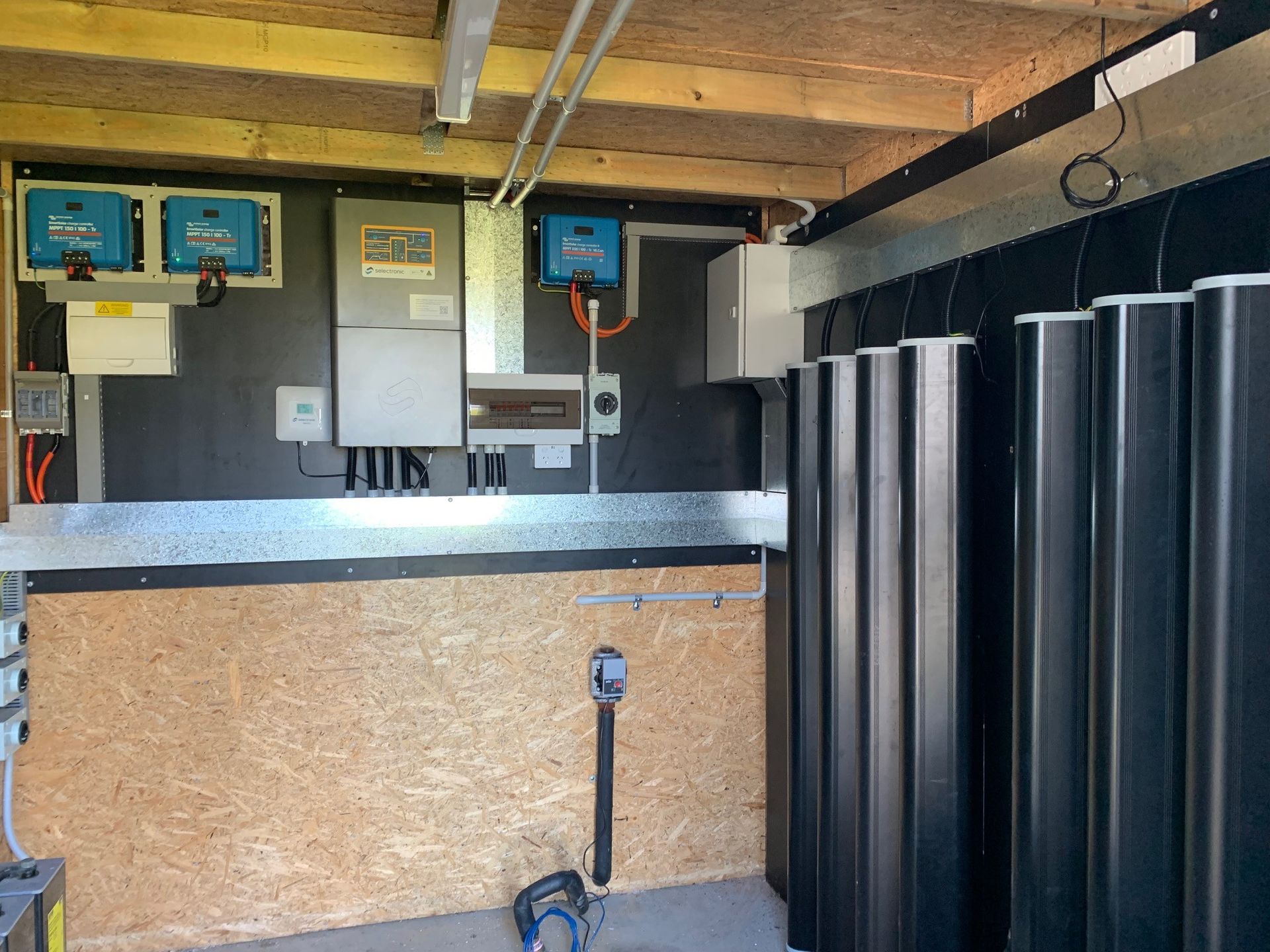 Indoor utility room with electrical panels, a workbench, and black storage bins along the wall