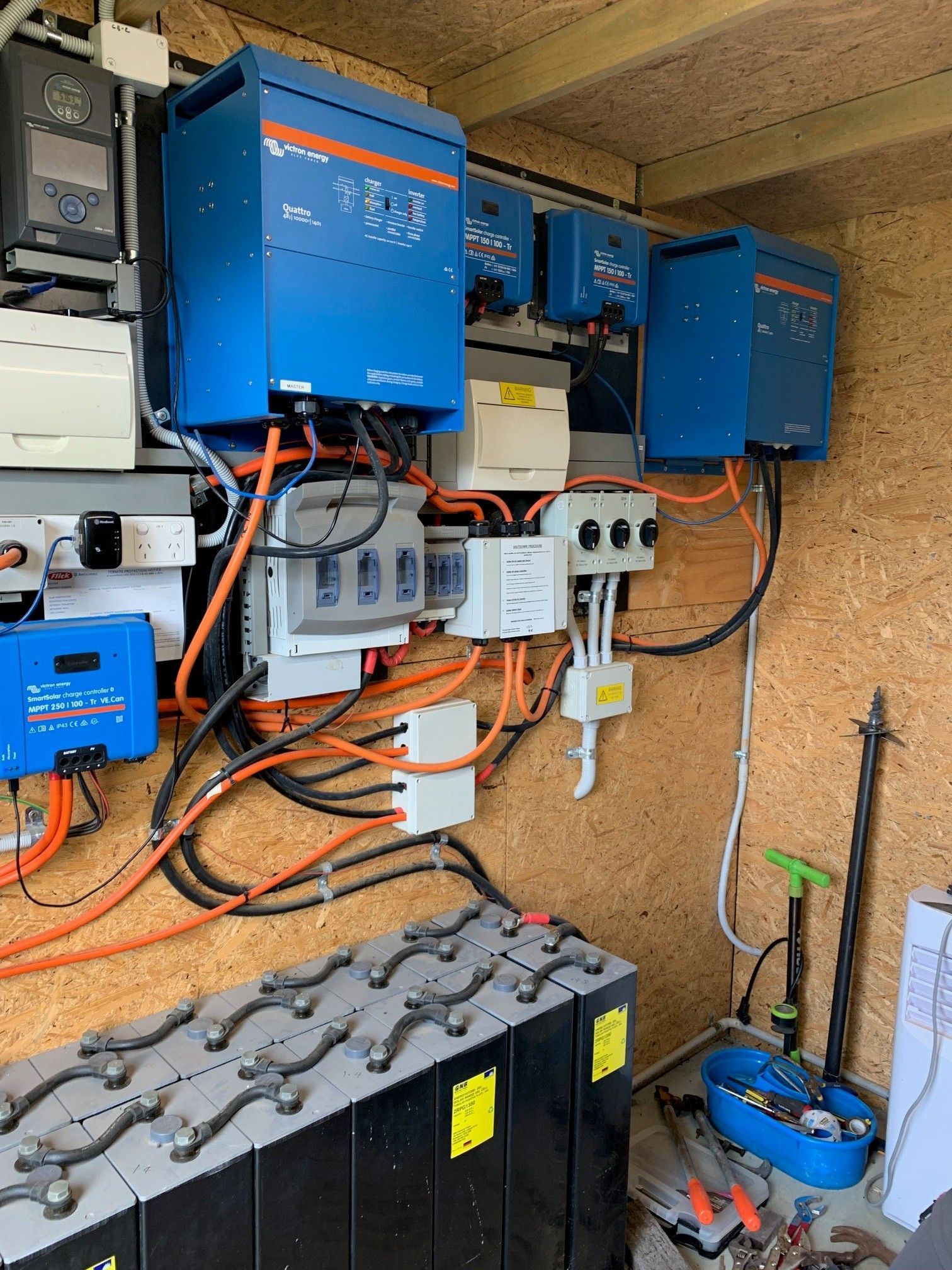Wall-mounted blue electrical inverters and wiring above a battery bank in a utility room