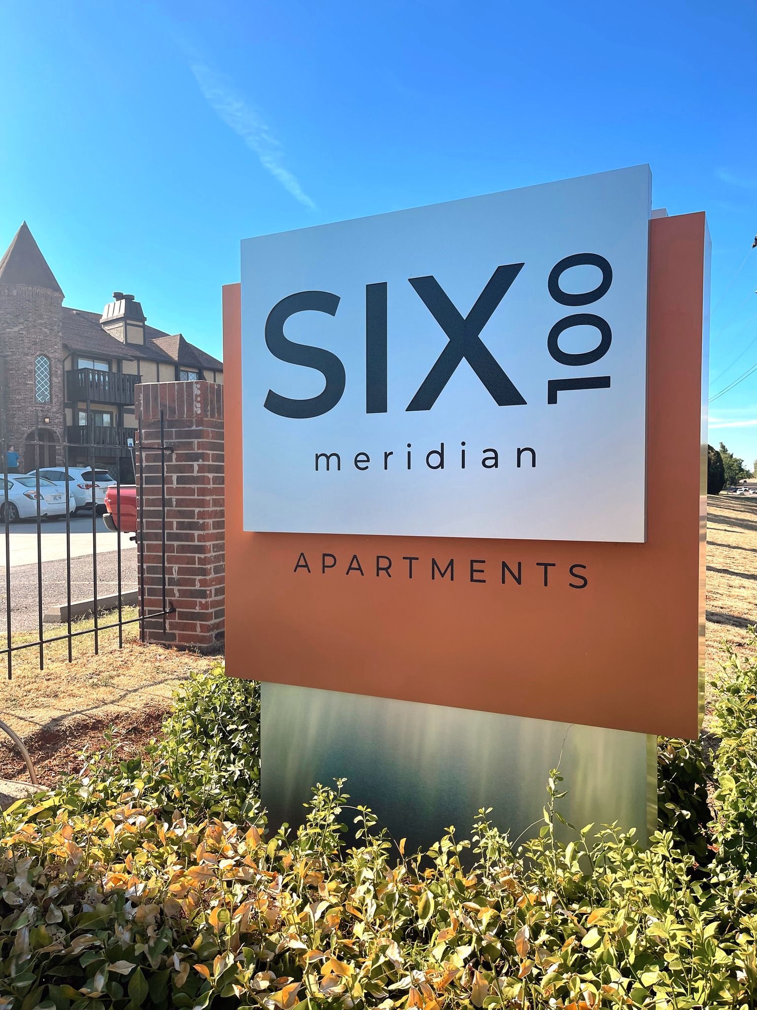 Sign for Six100 Meridian Apartments; white text on orange and silver panels, blue sky background.