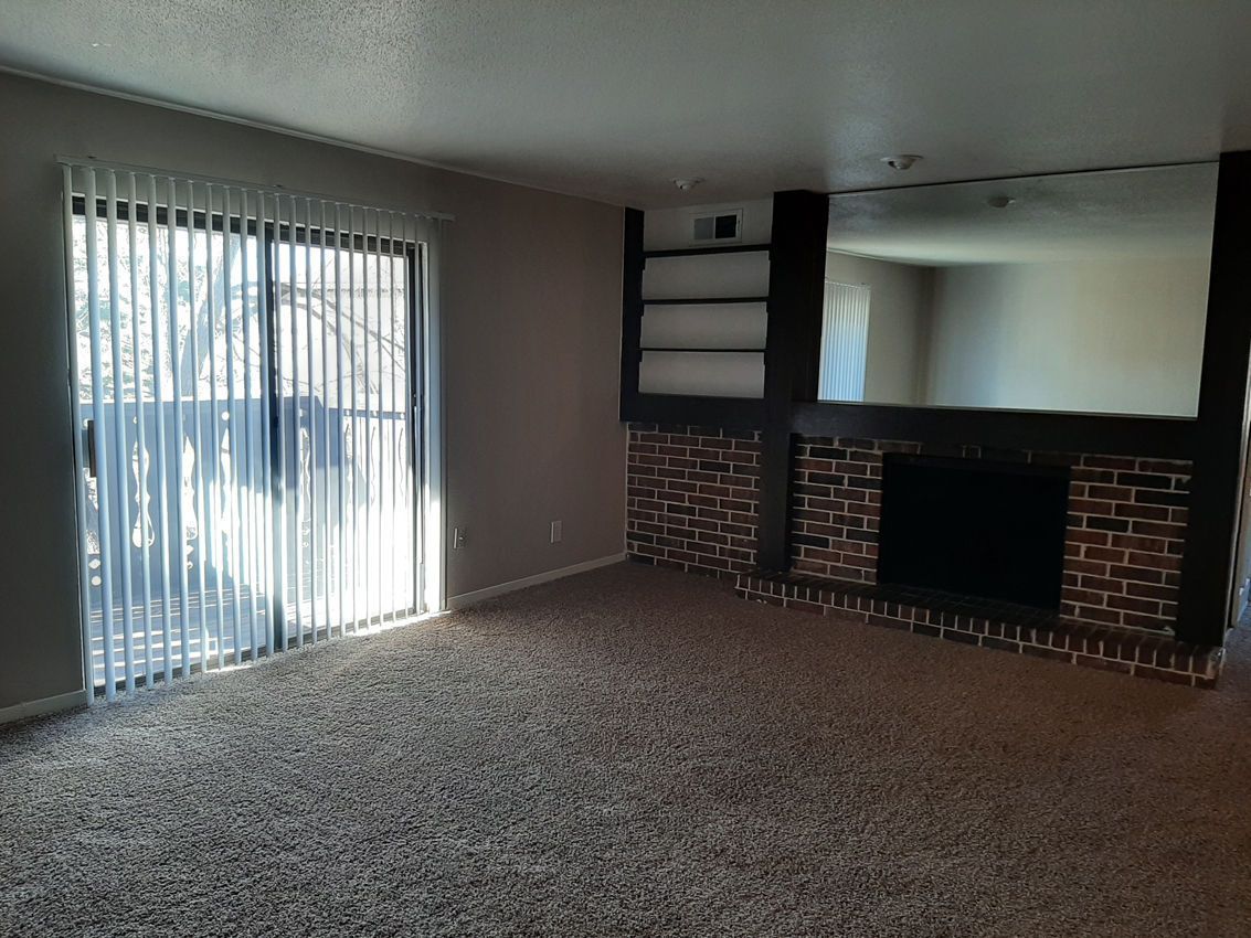 Empty living room with brick fireplace, large mirror, sliding glass door, and carpet.