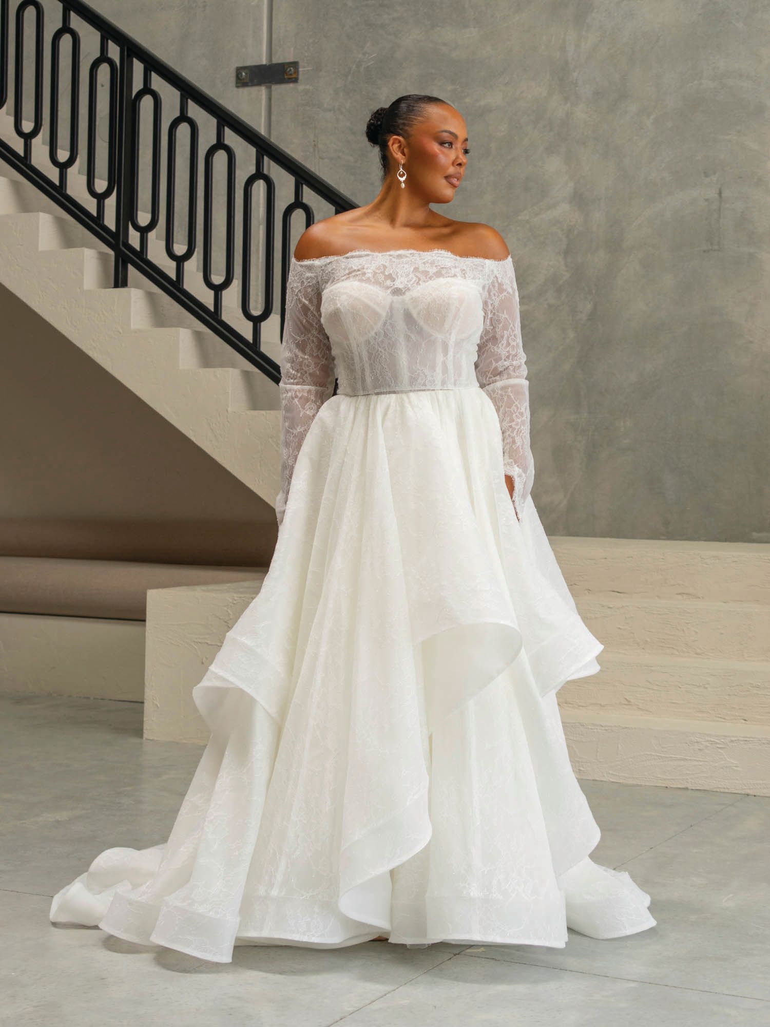A woman in a white wedding dress is standing in front of a staircase.