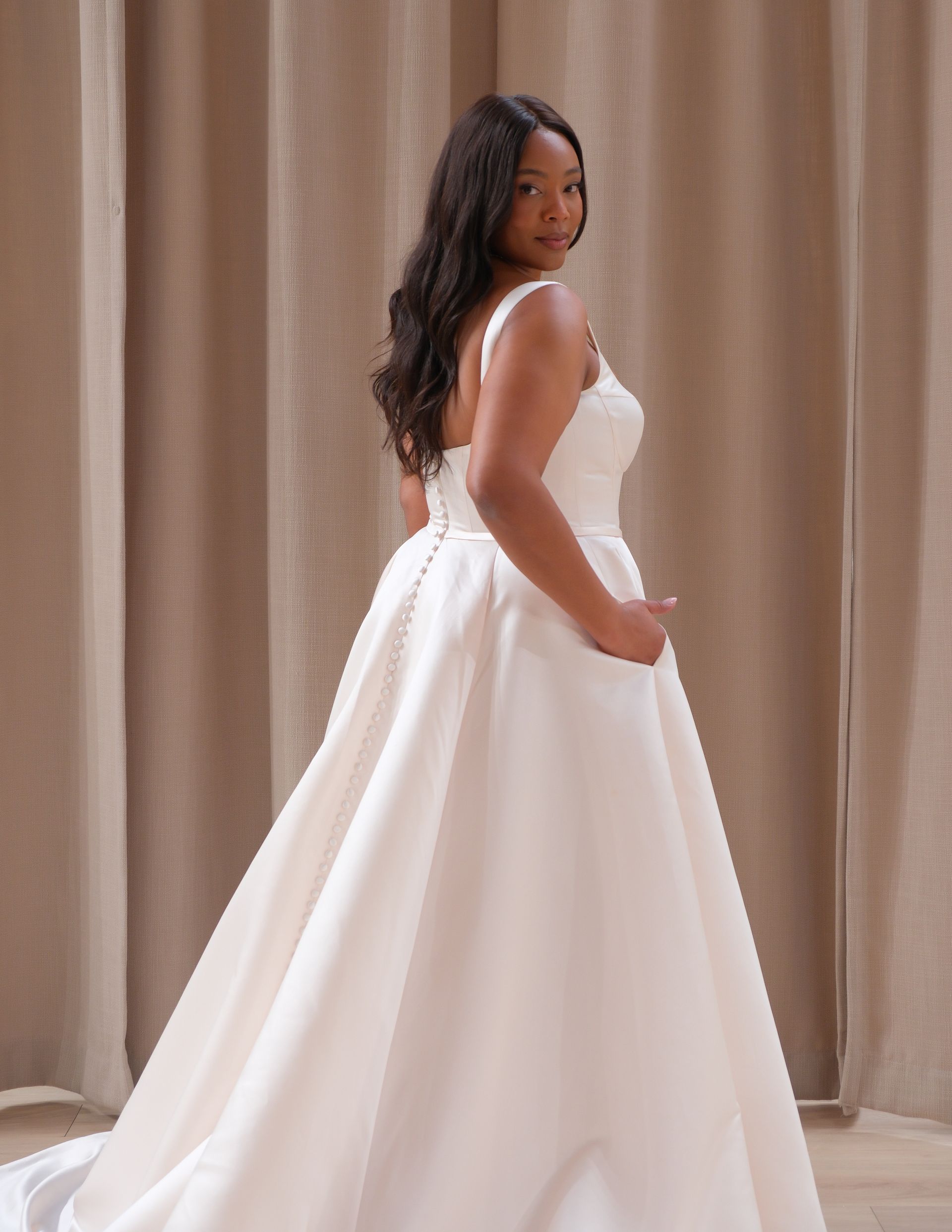 A woman in a white wedding dress is standing in front of a curtain.