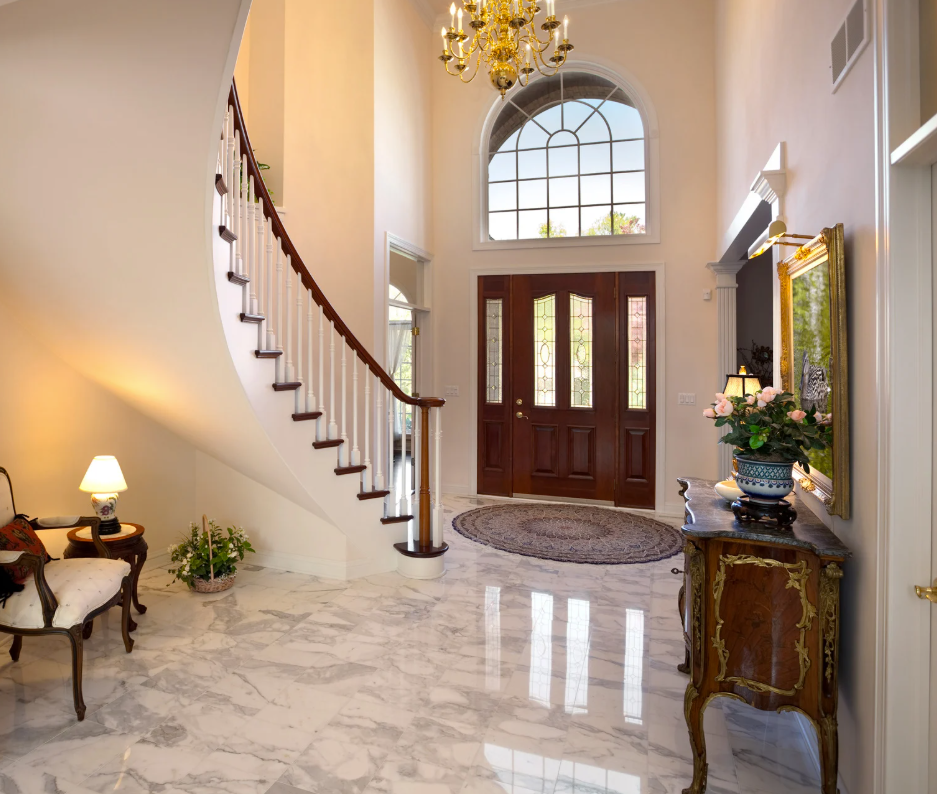 Elegant foyer with marble floor, curved staircase, and large wooden front door.