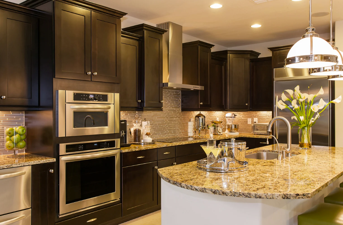 Dark brown kitchen cabinets with granite countertop island, stainless steel appliances, and decorative lighting.
