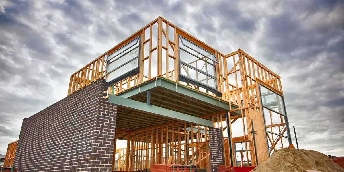 House under construction, wooden frame with brick facade, cloudy sky.