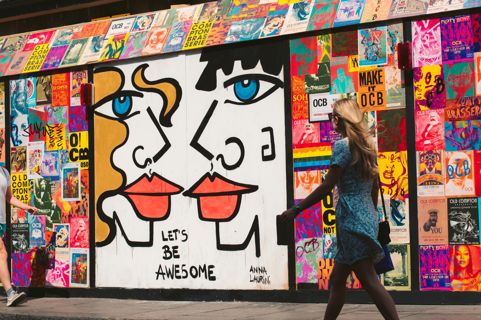 mujer caminando por la calle pasa por una pared llena de publicidad impresa de colores