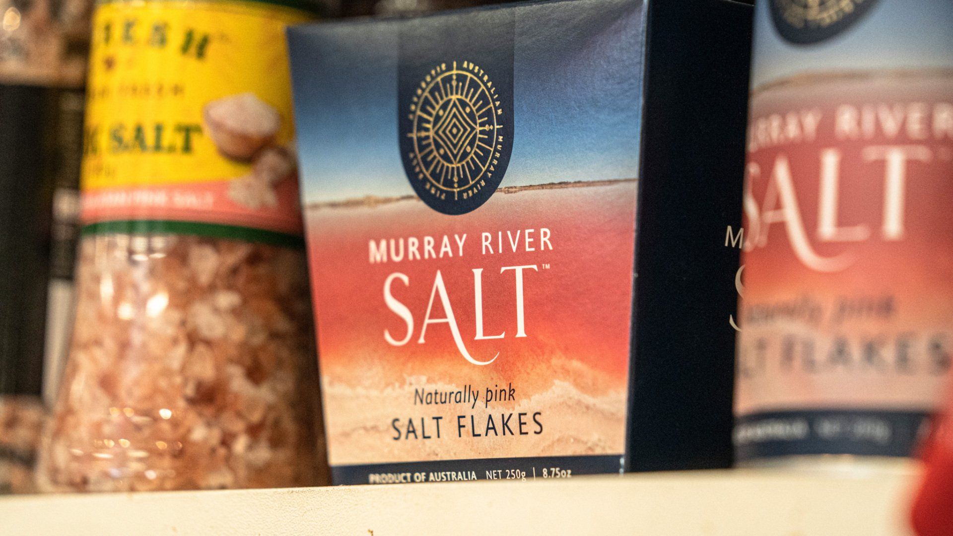 A box of murray river salt flakes is sitting on a shelf next to other salt flakes.