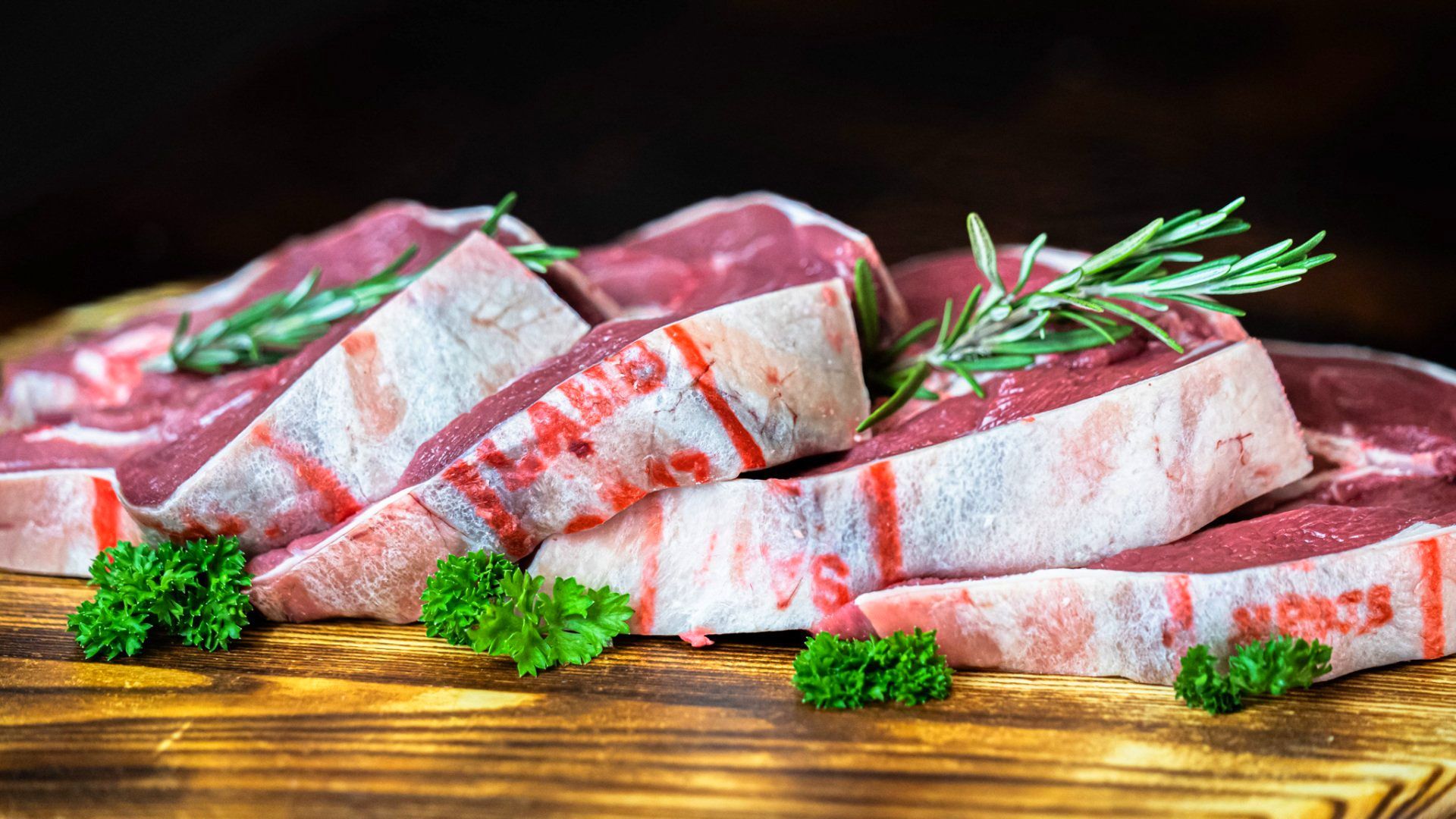 Two raw steaks are sitting on a wooden cutting board.