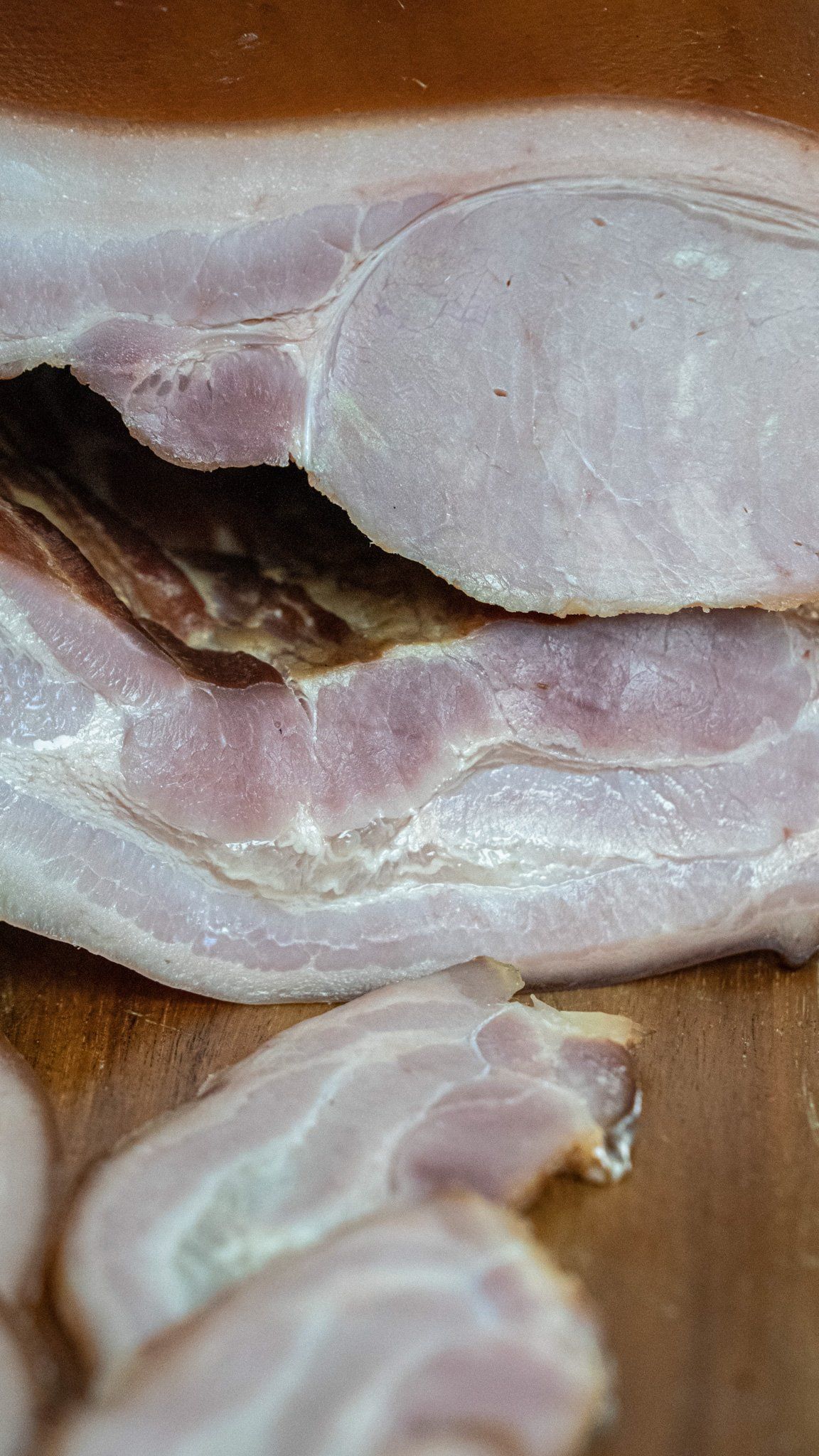 A close up of sliced bacon on a wooden cutting board.