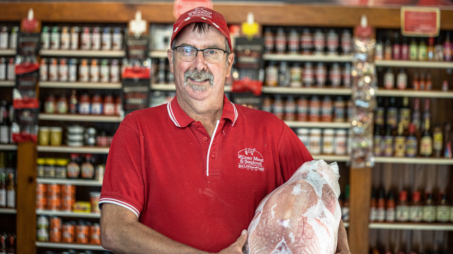 A man in a red shirt is holding a large piece of meat in front of a grocery store.