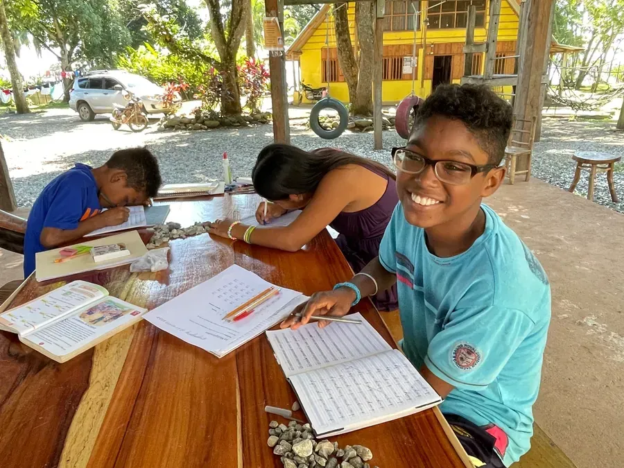 Children studying together at an outdoor classroom table with notebooks and pencils at  Casa Agua Azul.