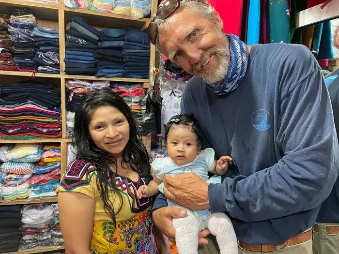 Volunteer holding a baby beside the child’s mother during a medical care visit at a community clothing shop
