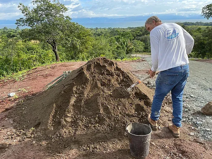 Man with a shovel moving dirt into a bucket with a shovel, scenic outdoor setting.