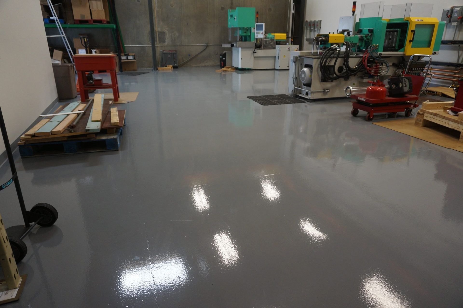 A shiny, gray industrial floor reflects overhead lights; machinery and equipment are visible in the background.