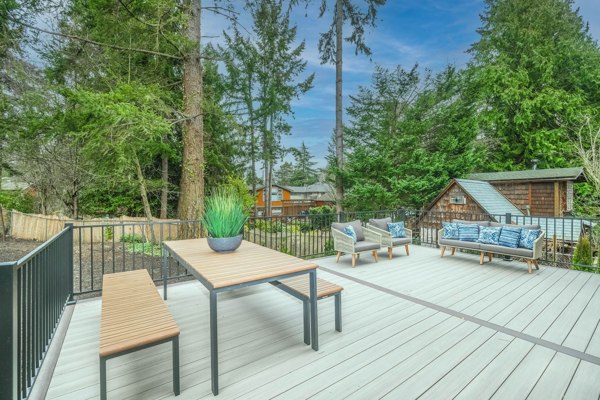 Wooden deck with outdoor dining set and seating, surrounded by trees.