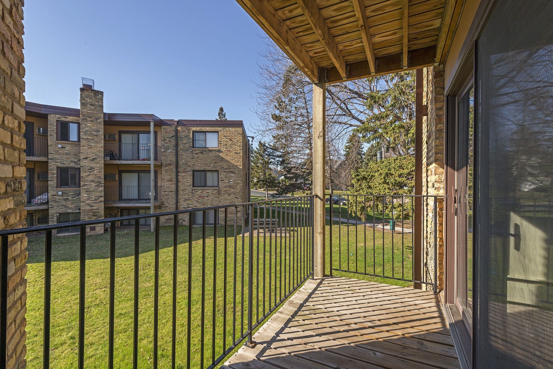 A balcony with a metal railing and a sliding glass door in front of a brick building.