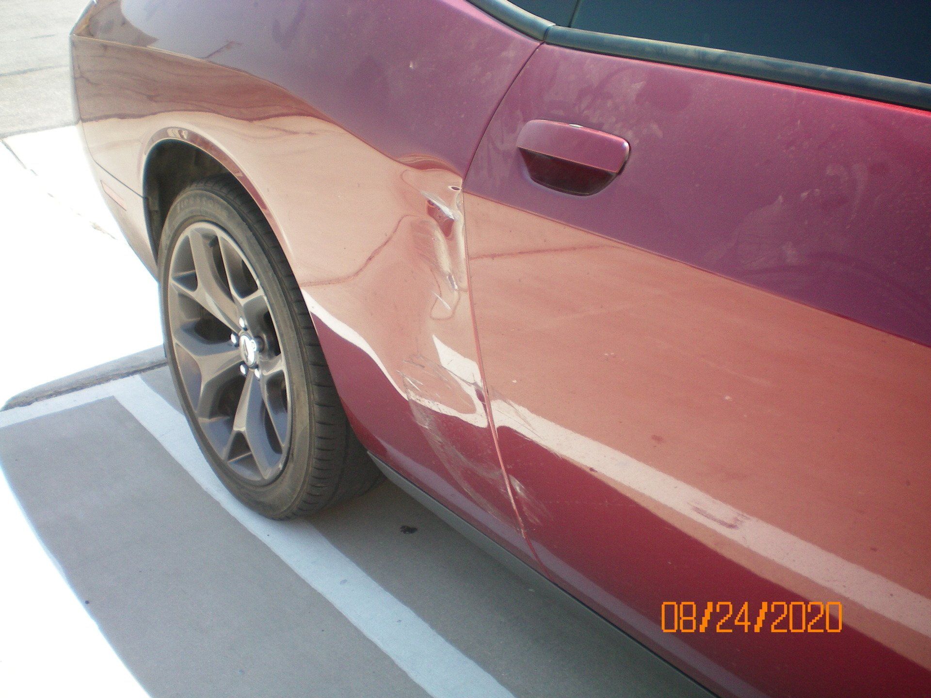 A red car with a damaged door is parked in a parking lot