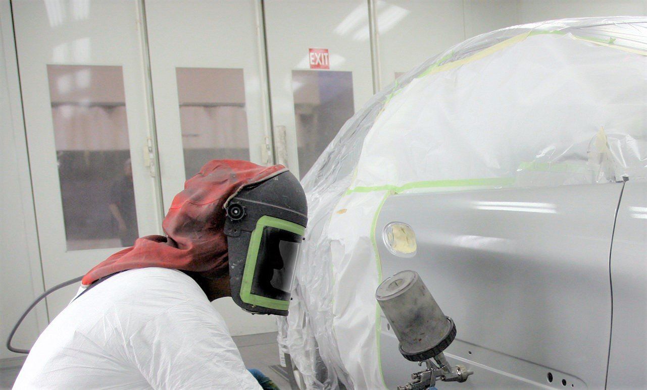 A man wearing a mask is painting a car in a garage.