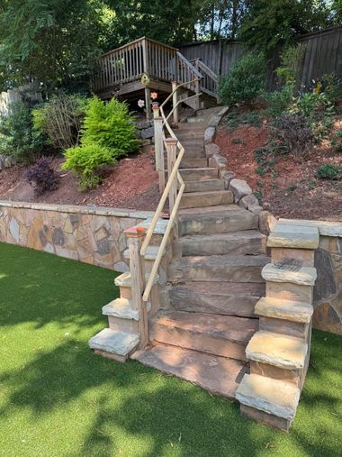 Stone steps with wooden handrail leading up a landscaped backyard hillside and deck