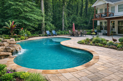 Curved backyard pool with blue water, stone patio, lounge chairs, and a house beside dense trees