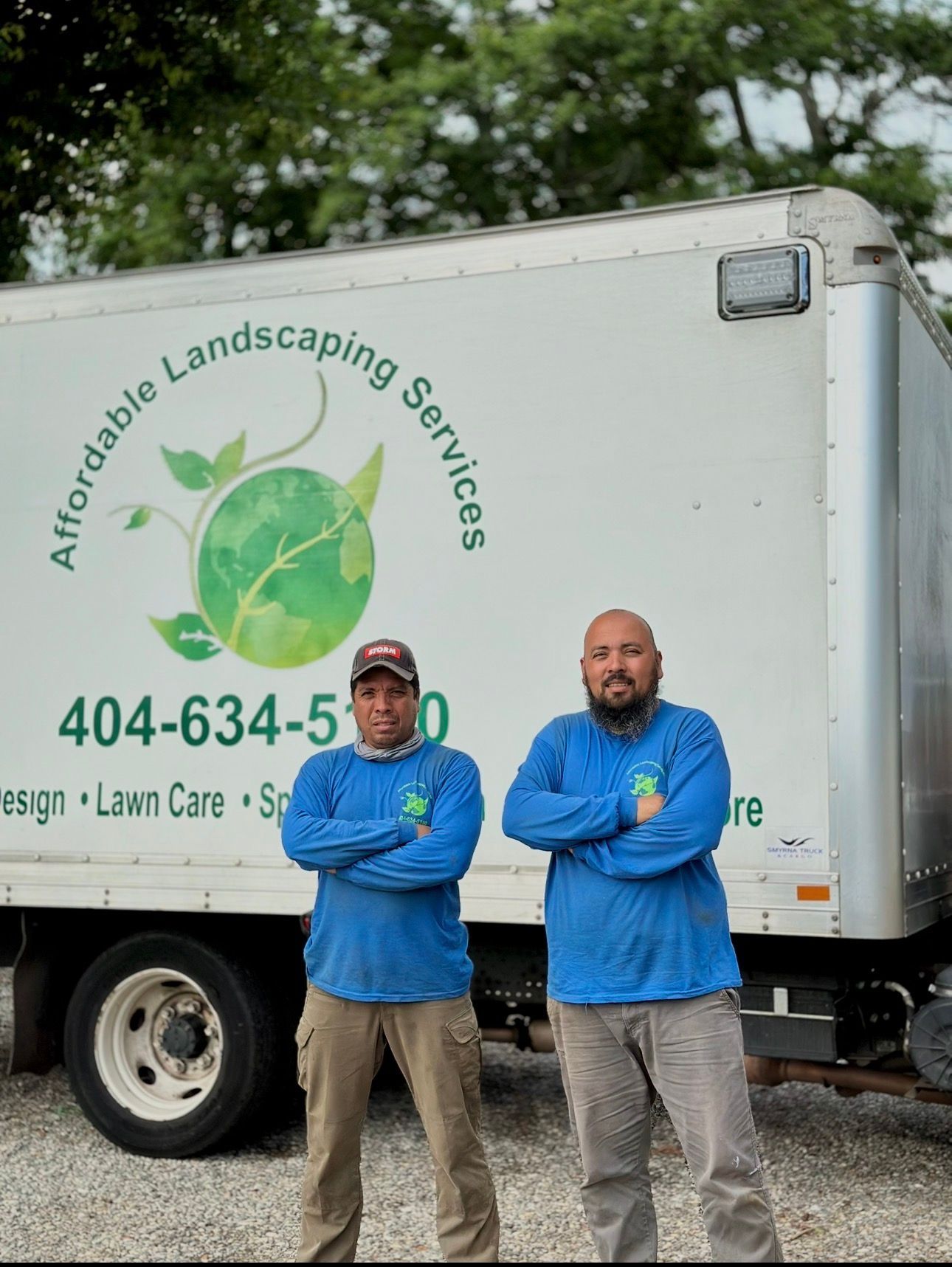 Two blue-jacketed workers standing in front of an Alfordable Landscaping Services truck.